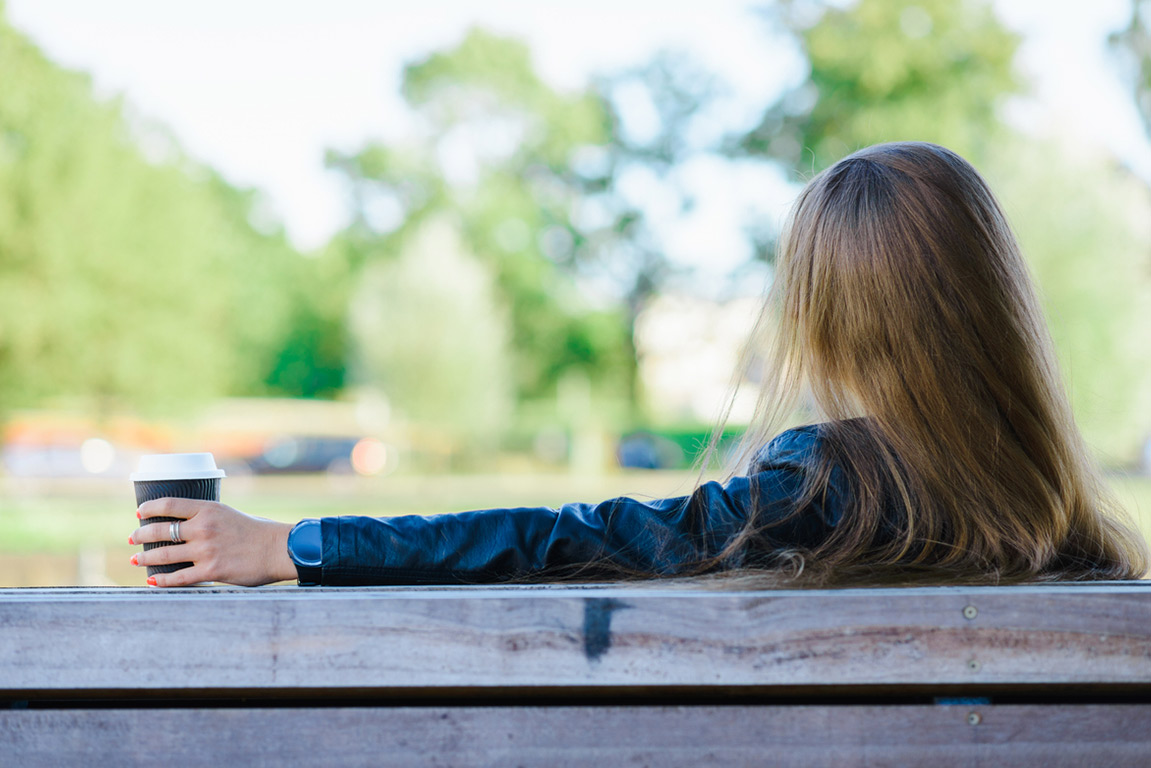 Woman relaxing outdoors with coffee, taking time to focus on her wellness